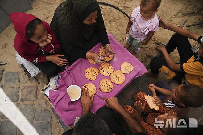 [칸유니스=AP/뉴시스] 11일(현지 시간) 가자지구 칸유니스에서 한 팔레스타인 피란민 가족이 밀가루 부족으로 렌틸콩을 갈아 만든 대체 빵을 먹고 있다. 2025.05.12.