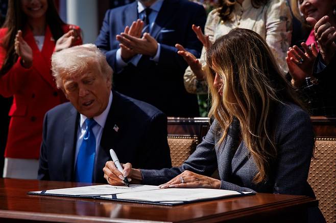 도널드 트럼프 미국 대통령이 19일(현지시간) 백악관 로즈가든에서 열린 리벤지 포르노 처벌 법안 서명식에서 아내 멜라니아 여사가 법안에 서명하는 모습을 지켜보고 있다. 연합뉴스