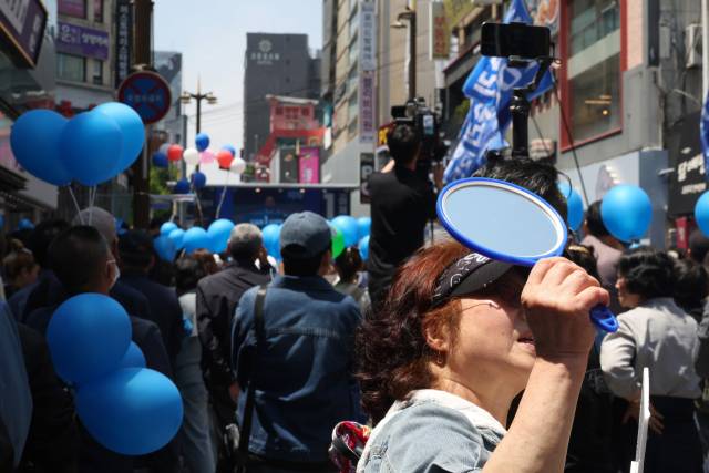 이재명 더불어민주당 대선 후보가 14일 부산 부산진구 서면거리에서 유권자들에게 지지를 호소하고 있는 가운데 지한 지지자가 저격수의 시야를 방해하기 위해 손거울을 들고 주변 건물을 향해 빛을 반사 시키고 있다. 부산=오승현 기자 2025.05.14