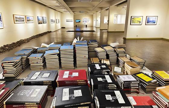 김영갑 20주기 전시회가 진행 중인 김영갑갤러리 두모악. 사진 아래에 쌓아놓은 노트가 2003년 갤러리를 열었을 때부터 모은 방명록이다.