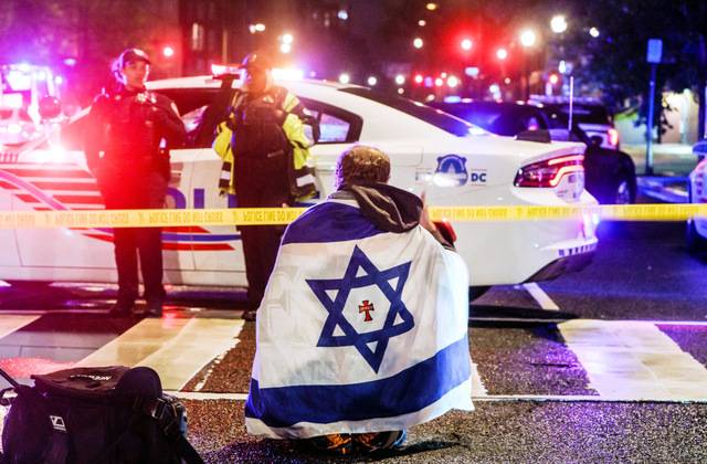 21일(현지시간) 이스라엘 대사관 직원 2명이 총격으로 사망한 현장인 워싱턴DC 유대인 박물관 인근에 폴리스라인이 설치돼 있고 그 앞에 이스라엘 국기를 두른 남성이 앉아 있다. EPA연합뉴스