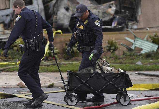 경찰들이 22일(현지시각) 미 샌디에이고 주택단지에서 발생한 소형비행기 추락사고 현장 인근에서 구조된 개를 안전한 곳으로 옮기고 있다. 샌디에이고/AP 연합뉴스