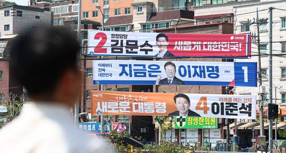 A passerby walks by banners of presidential cadidates ? Democratic Party's Lee Jae-myung, People Power Party's Kim Moon-soo and Reform Party's Lee Jun-seok ? in downtown Seoul on May 12. [NEWS1]