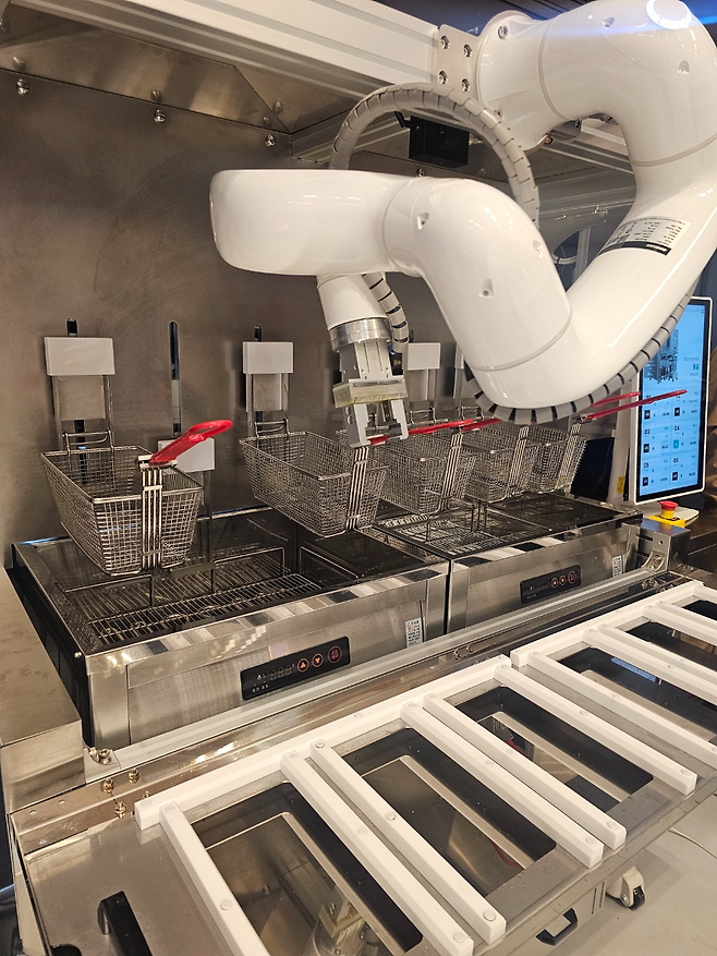 A frying robot developed by local robotics startup itcobot places a container into a deep fryer during a demonstration at the 2025 Food Service Fair at Coex in southern Seoul, April 29. (Choi Jae-hee/The Korea Herald)