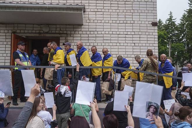24일 러시아와의 포로 교환에서 자국으로 돌아온 우크라이나 군인들이 국기를 몸에 감고 버스에서 내려 이동하고 있다. 실종자 가족들이 사진을 들고 이들에게 행방을 묻고 있다. AP 연합뉴스