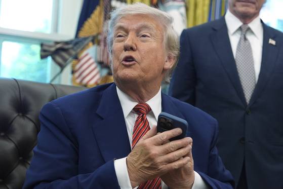 President Donald Trump holds his phone as he speaks to reporters after signing executive orders regarding nuclear energy in the Oval Office of the White House on May 23, 2025, in Washington. [AP/YONHAP]