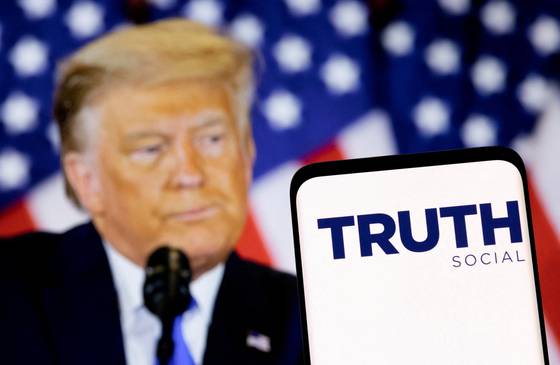 The Truth social network logo is seen on a smartphone in front of a display of U.S. President Donald Trump in this picture illustration taken on Feb. 21, 2022. [REUTERS/YONHAP]