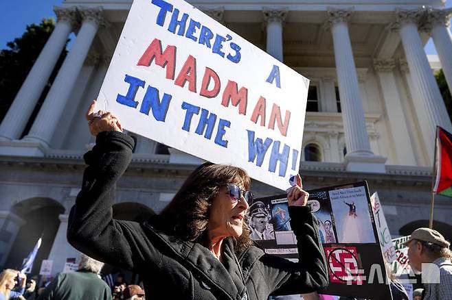 [새크라멘토=AP/뉴시스]  미 캘리포니아주 새크라멘토의 주 의사당 앞에서 한 여성이 "백악관에 웬 미친사람이 있다"는 손팻말을 들고 반트럼프 시위에 참여하고 있다.  2025.05.25.