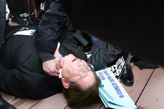 이재명 더불어민주당 후보가 지난해 1월 부산 가덕도 신공항 부지를 둘러본 후 기자들과 문답을 진행하던 중 왼쪽 목 부위에 습격을 당해 피를 흘린 채 쓰러져 있다. 부산=연합뉴스