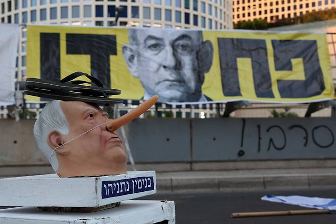 이스라엘 인질 석방을 요구하는 시위가 지난 24일(현지시간) 이스라엘 수도 텔아비브 이스라엘 국방부 청사 앞에서 열리고 있는 가운데 긴 코를 가진 베냐민 네타냐후 이스라엘 총리 인형 위에 샌들이 놓여 있다. [AFP]