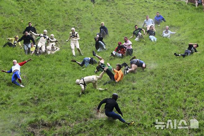 [브록워스=AP/뉴시스] 26일(현지 시간) 영국 글로스터셔주 브록워스의 쿠퍼스 힐에서 연례  치즈 굴리기 대회가 열려 남자부 참가자들이 언덕을 굴러 내려오고 있다. 이 대회는 약 180m 거리의 가파른 언덕에서 구르는 치즈를 잡아 결승선에 먼저 들어오는 사람이 우승하는 경기이다. 2025.05.27.