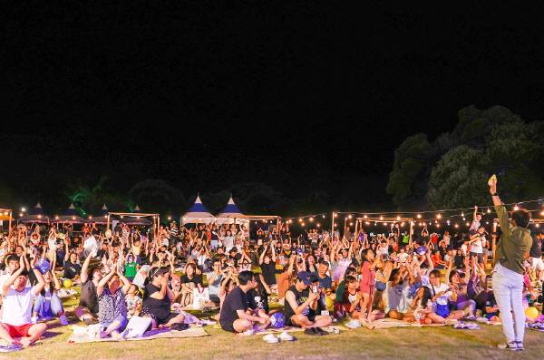 성밖숲 밤하늘 아래 모여든 수많은 가족과 관광객들이 '트윙클 성주!' 야간축제 현장에서 손을 높이 들고 즐겁게 호응하고 있다. -성주군-