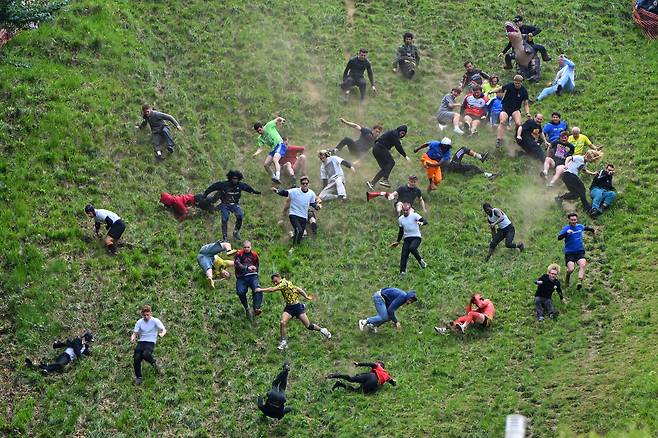 26일(현지 시각) 영국 글로스터셔주 브록워스의 쿠퍼스 힐에서 열린  연례 치즈 롤링 대회 남자 다운힐 레이스 부문에서 참가자들이 경쟁하고 있다./AP 연합뉴스