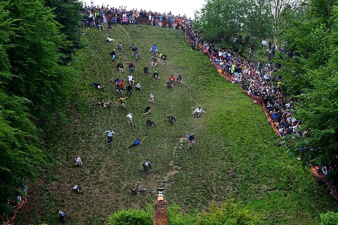 26일(현지 시각) 영국 글로스터셔주 브록워스의 쿠퍼스 힐에서 열린 연례 치즈 롤링 대회 남자 다운힐 레이스 부문에서 참가자들이 급경사 언덕을 내려오고 있다./AP 연합뉴스