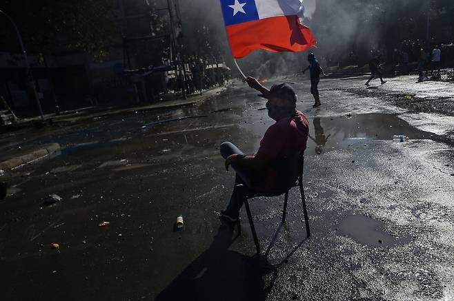 2019년 칠레 산티아고에서 열린 정부 비판 시위에서 한 시민이 거리에 의자를 깔고 앉아 칠레 국기를 흔들고 있다. Getty image/이매진스