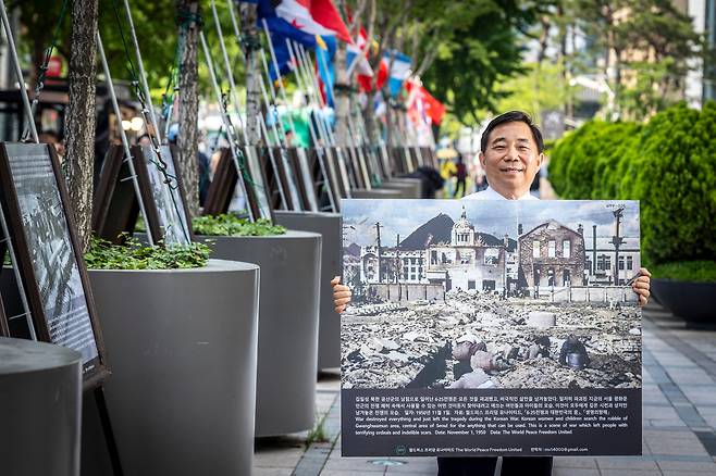 20년 동안 ‘6·25 사진전’을 이어온 안재철 ‘월드피스 프리덤 유나이티드(WPF)’ 대표가 지난 22일 서울 태평로 서울파이낸스센터 앞에서 전시 중인 사진 한 장을 들고 서 있다. 1950년 11월 철저히 파괴된 서울 광화문 근처의 폐허 속에서 사용할 수 있는 것을 찾으려고 애쓰는 여인들과 아이들의 모습. 6·25 때 파병한 16국을 포함해 우리나라를 도운 67국의 국기도 함께 전시한다. /이신영 영상미디어 기자