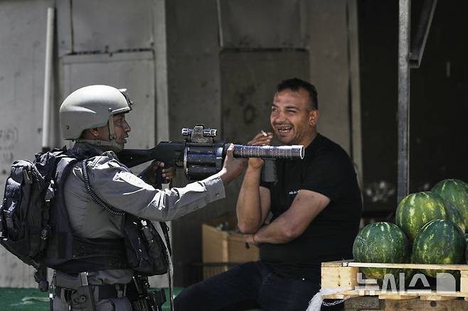 [나블루스=AP/뉴시스]5월 20일 요르단강 서안지구 나블루스 인근 아스카르 난민캠프에서 이스라엘군의 기습 작전이 벌어진 가운데, 한 이스라엘 국경 경찰이 수박 노점 옆에서 경비를 하고 있다. 2025.06.01.