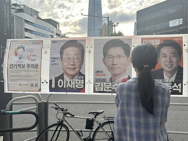 Office worker Kim, 30, looks at campaign posters of the three major presidential candidates — Lee Jae-myung of the Democratic Party of Korea, Kim Moon-soo of the People Power Party and Lee Jun-seok of the New Reform Party — in Songpa-gu, southern Seoul, Monday. (Lee Jung-joo/The Korea Herald)