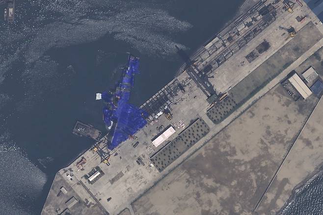 북한 조선중앙통신은 새로 건조한 5000톤급 구축함 진수식이 지난 21일 청진조선소에서 진행됐다며, “진수 과정에 엄중한 사고가 발생했다”고 보도했다. 사진은 위성으로 찍은 부서진 함정이 바다로 기울어진 장면. 북측이 위를 파란색 방수포로 보이는 위장막으로 덮은 상태다. [AP]