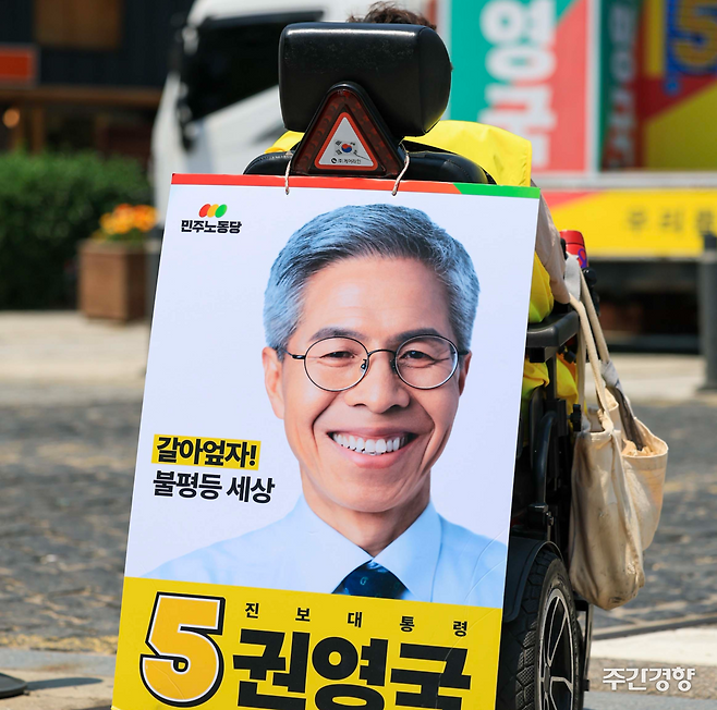 지난 5월 25일 권영국 대선 캠프의 유세지원차량 앞에서 한 장애인 지지자가 휠체어 뒤에 권영국 후보 사진을 걸고 유세에 참여하고 있다. 이준헌 기자.