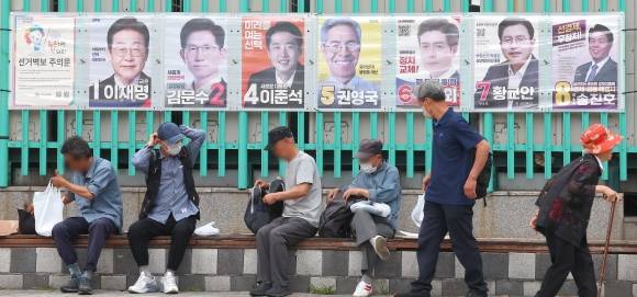 제21대 대통령 선거를 하루 앞둔 2일 인천 부평구 부평역 광장에 게시된 선거 후보들의 벽보 아래 시민들이 앉아 있다. 연합뉴스