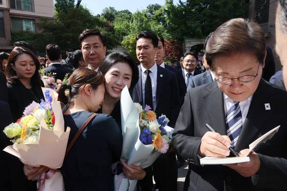 이재명 대통령과 김혜경 여사가 4일 인천 계양구 사저를 출발하다 이 대통령이 책에 서명을, 김 여사가 한 주민과 포옹을 하고 있다. 〈사진=연합뉴스〉