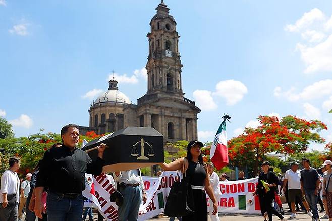 “사법부는 죽었다” 관 들고 시위 - 멕시코 사상 최초의 ‘판사 직선제’ 선거가 시작된 지난 1일 멕시코 할리스코주 과달라하라에서 시민들이 사법부를 상징하는 천칭이 그려진 관(棺)을 나르는 퍼포먼스를 펼치며 반대 시위를 벌이고 있다. 개표 결과 친여(親與) 인사들이 대법원을 장악할 것으로 예상돼 정권의 사법부 장악이란 우려가 현실화할 가능성이 커졌다. 이날 치러진 선거 투표율은 약 12%에 그쳤다. /EPA 연합뉴스