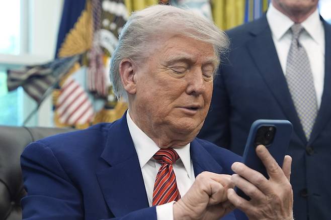 U.S. President Donald Trump silences his mobile phone, which rang twice, as he was speaking to reporters after signing executive orders regarding nuclear energy in the Oval Office on May 23 in Washington. [AP/YONHAP]