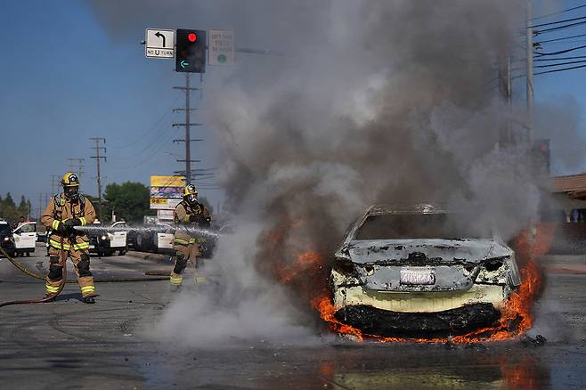 7일(현지 시간) 미국 캘리포니아주 로스앤젤레스에서 불법 체류자 체포에 반발하는 시위대의 방화로 불타는 차량을 소방대가 진화하고 있다. 2025.06.08 로스앤젤레스=AP/뉴시스