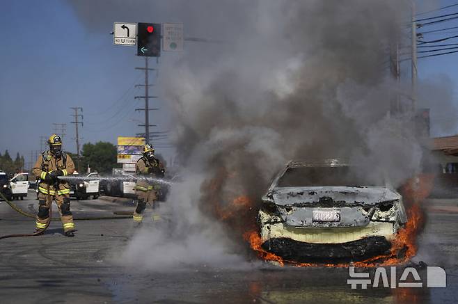 [로스앤젤레스=AP/뉴시스] 6월7일 LA 남부 시외의 교통요지인 콤프턴에서 연방 이민당국의 이민 체포 작전에 대항하는 시위대의 방화로 불타는 차량을 소방대가 진화하고 있다.  LA근교에 대한 이민국의 대대적 작전이 이틀째 이어지면서 국경수비대 병력과 시위대의 대치가 전쟁터를 방불케 했다. 2025. 06. 09.