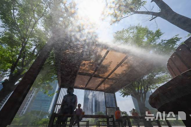 [서울=뉴시스] 황준선 기자 = 한낮 기온이 30도를 넘는 무더운 날씨를 보인 9일 오후 서울 여의도공원에서 시민들이 쿨링포그를 맞으며 휴식을 취하고 있다. 2025.06.09. hwang@newsis.com