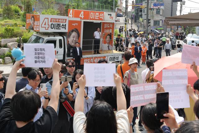 ▲개혁신당 이준석 대선 후보가 30일 서울 동작구 중앙대학교에서 유세 중인 가운데 일부 학생들이 최근 이 후보의 TV토론 여성 신체 관련 발언을 규탄하며 팻말을 들고 있다. ⓒ연합뉴스