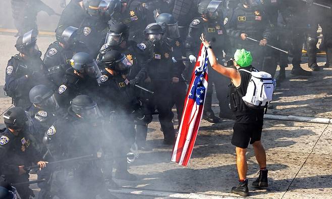 8일 미국 캘리포니아주 로스앤젤레스 도심에서 연방정부의 이민 단속에 반대하는 시위 중, 시위 참가자가 캘리포니아주 고속도로순찰대원(CHP)들과 마주 서서 미국 국기를 들어 보이고 있다. 로이터 연합뉴스