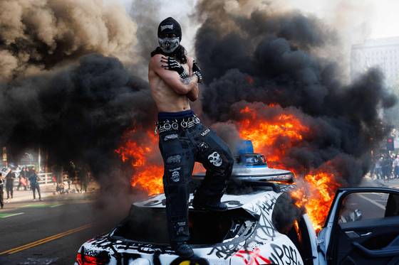 지난 8일 LA 도심 시위 현장에서 불에 타는 차량 위에 한 시위자가 올라가 있다. AFP=연합뉴스