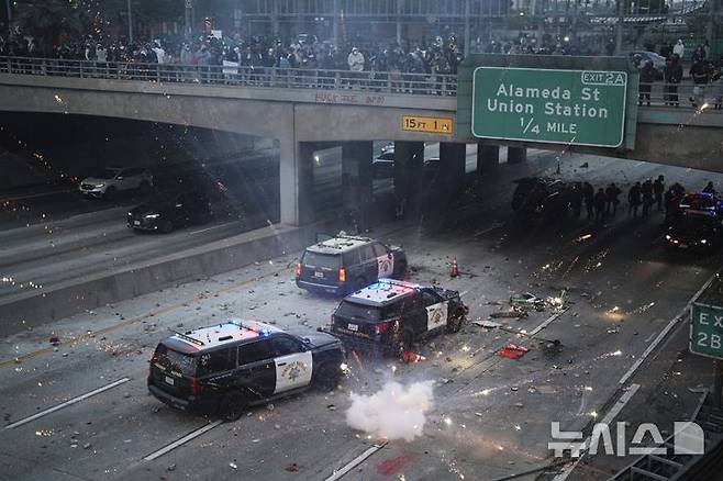 [로스앤젤레스=AP/뉴시스] 8일(현지 시간) 미 캘리포니아주 로스앤젤레스 도심 메트로폴리탄 구치소 인근 101번 고속도로에서 이민세관단속국(ICE)의 불법 이민자 단속 및 체포에 항의하는 시위대가 경찰차를 향해 돌을 던지고 섬광탄을 터트리고 있다. 2025.06.09.