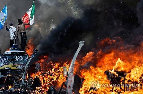LA에서 차량이 불타고 있는 가운데 깃발을 든 불법이민자 단속 반대 시위대  [AFP=연합뉴스 자료사진. 재판매 및 DB금지]