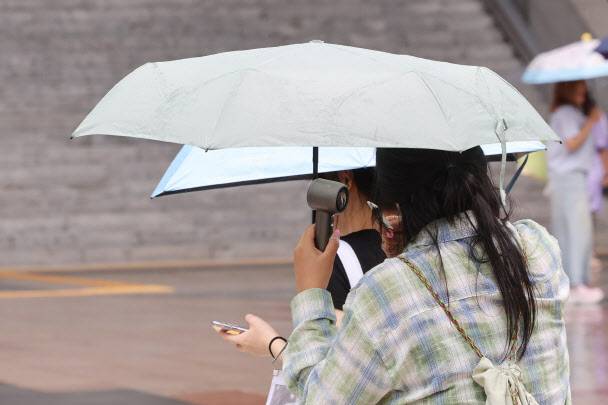 서울 용산역광장에서 우산을 쓴 시민이 휴대용 선풍기를 사용하며 이동하고 있다.(사진=연합뉴스)