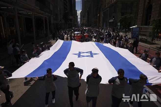 [뉴욕=AP/뉴시스] 18일(현지 시간) 미국 뉴욕의 맨해튼 5번가에서 열린 ‘이스라엘의 날'(Israel Day on 5th) 퍼레이드에 참가자들이 대형 이스라엘 국기를 들고 행진하고 있다. '이스라엘의 날' 퍼레이드는 뉴욕에서 미국 내 유대인 공동체와 이스라엘의 연대를 강조하기 위해 열리는 연례행사이다. 2025.05.19.