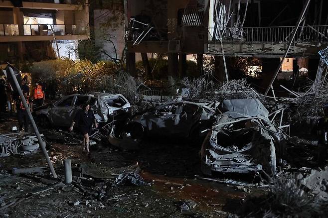 13일(현지시각) 이스라엘 텔아비브에서 한 여성이 이란이 발사한 미사일로 파손된 건물 앞에서 불에 탄 차량 사이를 걷고 있다. 텔아비브/AFP 연합뉴스