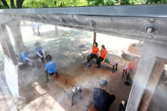 As Seoul’s daytime high hit 31 degrees Celsius (88 degrees Fahrenheit), signaling the arrival of early summer heat, people in Yeouido Park, Yeongdeungpo District, western Seoul, seek relief by sitting under cooling fog machines to beat the sweltering weather on June 12. [NEWS1]