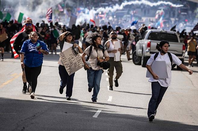 2025년 6월 14일, 워싱턴 D.C.에서 트럼프 대통령의 군사 퍼레이드가 열린 날, 로스앤젤레스에서 열린 ‘노 킹스(No Kings)’ 시위 도중 당국이 불법 집회를 선언한 뒤 충돌이 발생하자 시위자들이 달아나고 있다. ‘노 킹스’ 시위대는 뉴욕, 로스앤젤레스, 시카고, 필라델피아, 휴스턴, 애틀랜타를 포함한 수백 개 도시 거리로 나서 트럼프 대통령의 독재적 권력 남용이라 부르는 행보를 규탄했다. [사진 = AFP 연합뉴스]