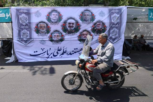 이스라엘의 이란 공습으로 이란의 주요 군 지도자 및 핵물리학자들이 사망한 다음날인 14일 이란 테헤란의 한 거리에서 한 남성이 전날 사망한 인물들을 추모하는 현수막이 걸린 담벼락 앞을 오토바이를 타고 지나가고 있다. AFP 연합뉴스