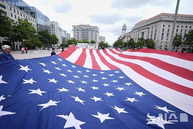 [워싱턴=AP/뉴시스] 14일(현지 시간) 미국 워싱턴 자유의 광장에서 시민들이 미 육군 창설 250주년 기념 열병식이 열리기에 앞서 대형 성조기를 펼쳐 들고 있다. 이날은 도널드 트럼프 대통령의 79번째 생일이기도 하다. 2025.06.15.