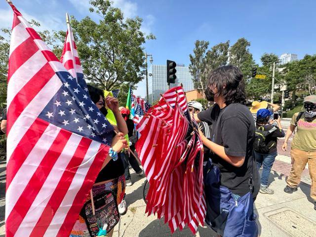 14일 미국 캘리포니아주 로스앤젤레스 시청 앞 광장에서 '노 킹스' 시위가 진행 중인 가운데 미국 시민권자인 크리스가 위아래가 뒤집힌 성조기'를 시위자들에게 나눠주고 있다. 거꾸로 뒤집은 국기는 미국이 심각한 위험에 처해 있다는 경고의 의미를 담고 있다. 로스앤젤레스=이서희 특파원