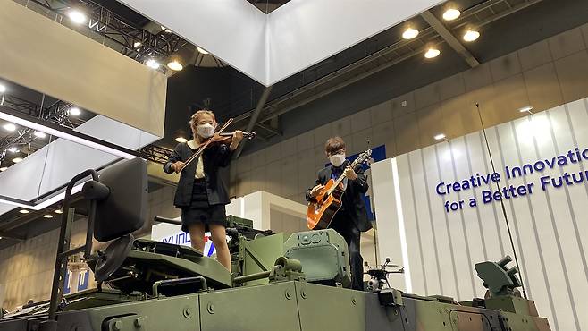 2022년 9월22일 반전 운동가들이 대한민국 방위산업전에 전시된 장갑차에 올라가 바이올린을 연주하고 있다. ⓒ전쟁없는세상 제공