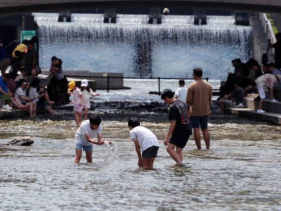People cool off by dipping their feet in the water at Cheonggyecheon in central Seoul on June 17. [NEWS1]