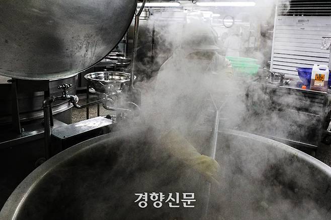 한 급식 조리사가 큰 솥 앞에 서서 뜨거운 김을 맞으며 조리용 삽으로 돼지갈비찜을 뒤집고 있다. 성동훈 기자