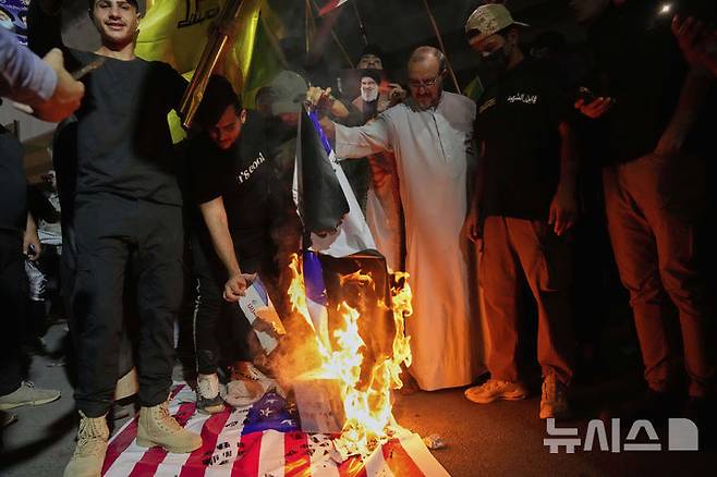 [바그다드=AP/뉴시스] 16일(현지 시간) 이라크 바그다드에서 시위대가 미국 대사관이 있는 그린존으로 이어지는 다리에 모여 이스라엘의 이란 공습에 항의하며 이스라엘과 미국 국기를 불태우고 있다. 2025.06.17.