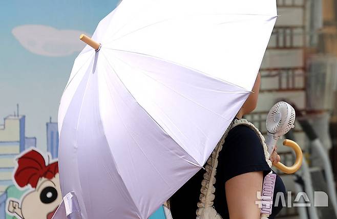 [대구=뉴시스] 이무열 기자 = 전국이 30도 안팎의 무더운 날씨를 보인 19일 대구 중구 동성로에서 한 시민이 양산과 손 선풍기를 들고 길을 걷고 있다. 2025.06.19. lmy@newsis.com