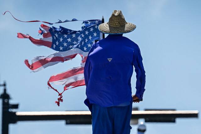 밀짚모자를 쓴 농부 차림의 한 미국인이 지난 14일(현지시간) 플로리다주 팜비치에 위치한 도널드 트럼프 대통령의 마러라고 사저 근처에서 열린 ‘노 킹스(No Kings)’ 시위에 참가해 찢어진 성조기를 들고 서 있다. 노 킹스 시위는 트럼프 대통령이 자신의 생일인 이날 수도 워싱턴DC에서 군사 퍼레이드를 벌이자 ‘당신은 왕이 아니다’는 구호와 함께 미국 전역에서 벌어졌다. AFP연합뉴스
